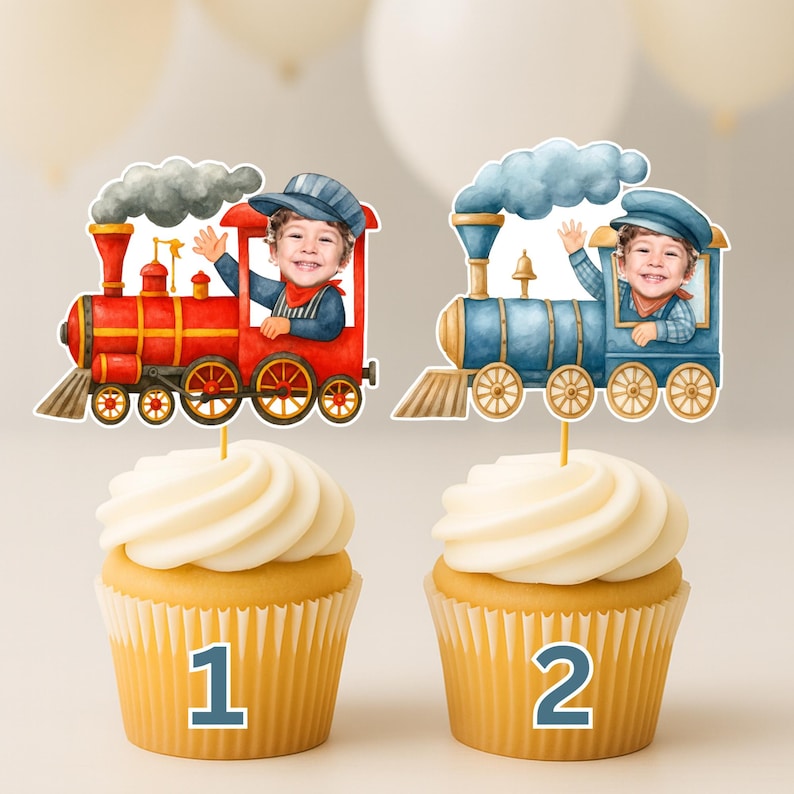 May include: Two cupcakes topped with personalized train-themed cake toppers. One topper features a red steam engine with a child's photo, the other a blue steam engine with a child's photo. Both trains have smoke clouds and are labeled 1 and 2.