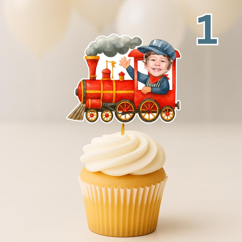 May include: A cupcake topper featuring a red steam locomotive with a gray smoke plume and a cutout of a smiling child wearing a blue cap and shirt, positioned in the train cabin, all mounted on a thin stick inserted into a frosted cupcake.