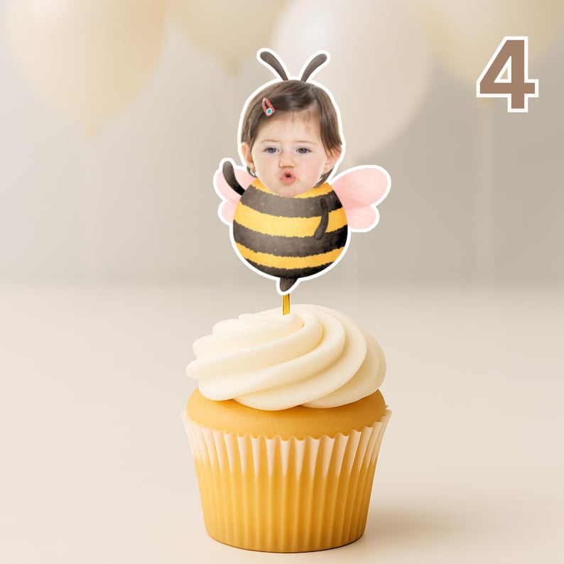 May include: A cupcake with white icing and a yellow paper case. A bee-themed topper with a child's face, black and yellow stripes, and pink wings. The number 4 is visible in the background.