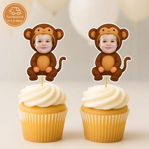 Op de afbeelding: Twee cupcakes met gele vormpjes en witte glazuur. Elke cupcake is versierd met een aap-thema decoratie met het gezicht van een kind. De decoraties zijn bruin en beige. De afbeelding bevat een cirkelvormige afbeelding met tekst.
