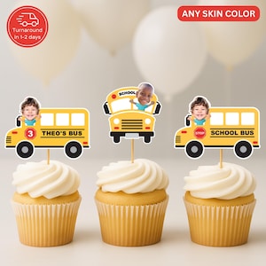 May include: Three cupcakes topped with yellow school bus toppers featuring children's faces. The toppers are yellow with black wheels and the text "THEO'S BUS" and "SCHOOL BUS". The cupcakes have white frosting.