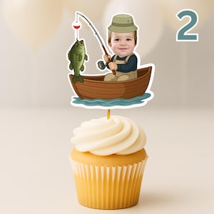 K&ouml;nnte beinhalten: Ein Cupcake-Topper mit einer Cartoon-Illustration eines Kindes mit beigem Fischerhut, das in einem braunen Holzboot sitzt und eine Angelrute mit einem gr&uuml;nen Fisch an der Schnur h&auml;lt. Der Topper ist auf einem d&uuml;nnen St&auml;bchen im Cupcake befestigt.