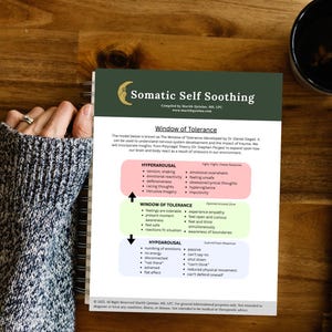 May include: A printed document titled "Somatic Self Soothing" with the text "Window of Tolerance." The document lists emotional states and responses, including hyperarousal, hypoarousal, and the optimal arousal zone. The document is on a wooden surface.