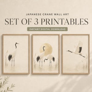 May include: A set of three wall art printables featuring Japanese cranes in a neutral beige palette. The text reads JAPANESE CRANE WALL ART SET OF 3 PRINTABLES INSTANT DIGITAL DOWNLOAD. Each print depicts cranes in water with reeds and a sun.