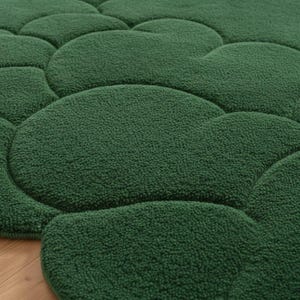 Puede incluir: Primer plano de una alfombra verde texturizada con un dise&ntilde;o &uacute;nico en forma de guijarros. La superficie de la alfombra es de un verde bosque profundo, con una textura suave y afelpada. El dise&ntilde;o presenta formas redondeadas e interconectadas, creando un patr&oacute;n visualmente interesante.
