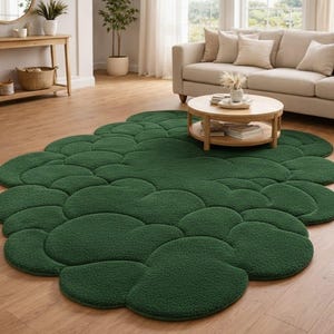 Puede incluir: Una alfombra verde oscuro con forma de nube. La alfombra est&aacute; hecha de un material suave y texturizado y tiene un dise&ntilde;o org&aacute;nico &uacute;nico. La alfombra est&aacute; colocada sobre un suelo de madera en un sal&oacute;n.