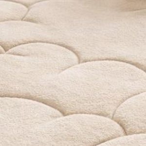 Puede incluir: Primer plano de un protector de colch&oacute;n acolchado beige con un patr&oacute;n en forma de nube. La tela tiene un aspecto suave y texturizado. Las costuras crean una serie de formas redondeadas e interconectadas en la superficie.