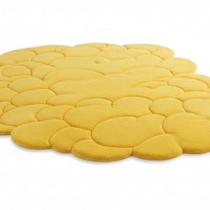 Puede incluir: Una alfombra amarilla con forma de nube y superficie texturizada. La alfombra est&aacute; formada por varias formas redondeadas interconectadas, creando un dise&ntilde;o &uacute;nico y moderno. La alfombra es de color amarillo c&aacute;lido.