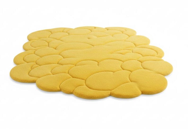 Puede incluir: Una alfombra amarilla con forma de nube y superficie texturizada. La alfombra est&aacute; formada por varias formas redondeadas interconectadas, creando un dise&ntilde;o &uacute;nico y moderno. La alfombra es de color amarillo c&aacute;lido.