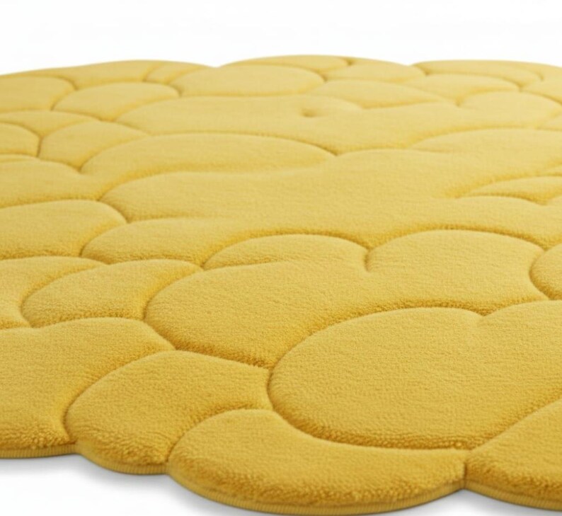 Puede incluir: Primer plano de una alfombra de ba&ntilde;o amarilla con un dise&ntilde;o de guijarros. La alfombra est&aacute; hecha de un material suave y afelpado y tiene una superficie texturizada. El color es un amarillo c&aacute;lido y soleado.