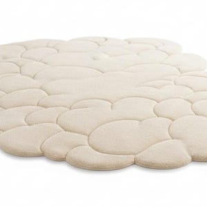 Puede incluir: Una alfombra beige con forma de nube y superficie texturizada. La alfombra est&aacute; compuesta por m&uacute;ltiples formas redondeadas e interconectadas, creando una apariencia suave y afelpada. La alfombra est&aacute; dise&ntilde;ada para la decoraci&oacute;n del hogar y a&ntilde;ade un toque de confort a cualquier habitaci&oacute;n.