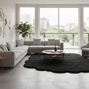 Puede incluir: Un sal&oacute;n moderno con un sof&aacute; seccional gris, una mesa de centro redonda de madera y una alfombra negra con forma de nube. La habitaci&oacute;n tiene grandes ventanales con vistas a la ciudad, un sill&oacute;n gris y obras de arte enmarcadas.