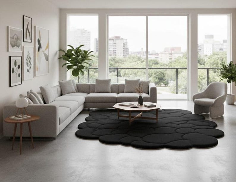 Puede incluir: Un sal&oacute;n moderno con un sof&aacute; seccional gris, una mesa de centro redonda de madera y una alfombra negra con forma de nube. La habitaci&oacute;n tiene grandes ventanales con vistas a la ciudad, un sill&oacute;n gris y obras de arte enmarcadas.
