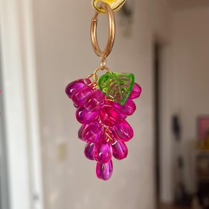 Puede incluir: Pendiente de aro dorado con un racimo de cuentas rosas en forma de uva y un dije de hoja verde. Las cuentas translúcidas tienen un acabado brillante. Accesorio único hecho a mano.