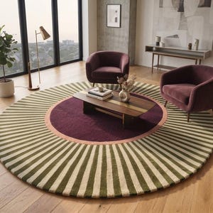 May include: A large circular area rug featuring a central deep purple circle surrounded by a thin peach-colored ring and an outer border of radiating olive green and cream-colored stripes. The rug is placed on a light-toned wooden floor.