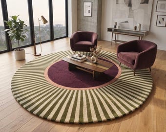 May include: A large circular area rug featuring a central deep purple circle surrounded by a thin peach-colored ring and an outer border of radiating olive green and cream-colored stripes. The rug is placed on a light-toned wooden floor.