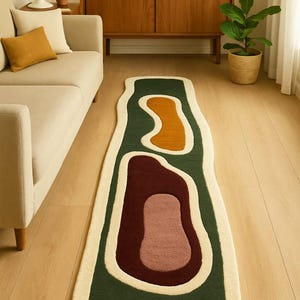 Può includere: Un tappeto lungo di forma astratta con una combinazione di colori verde, ruggine e bordeaux, con un bordo color crema. Il design del tappeto è organico e moderno. Si trova su un pavimento in legno in un soggiorno. Le dimensioni del tappeto sono in centimetri.