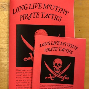 Könnte beinhalten: Zwei rote Broschüren mit schwarzem Text und Illustrationen. Der Text auf den Broschüren lautet "Long Live Mutiny Pirate Tactics". Die Illustrationen zeigen einen Totenkopf und gekreuzte Knochen.