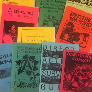Puede incluir: Una colección de nueve pequeños libros de bolsillo coloridos con títulos como "Colonización y Descolonización", "Patriotismo: Una Amenaza para la Sociedad", "Código de Honor", "Cortocircuito", "Traer la Guerra a Casa", "Construcción y Uso de Contadores Geiger", "Sembrando las Semillas de la Revolución", "Guía de Supervivencia de Acción Directa" y "Combate Mano a Mano".