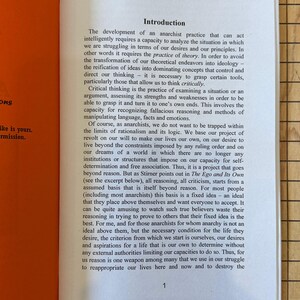 May include: An open book with a bright orange cover and white pages. The text on the page is about the development of anarchist practice and the importance of critical thinking.