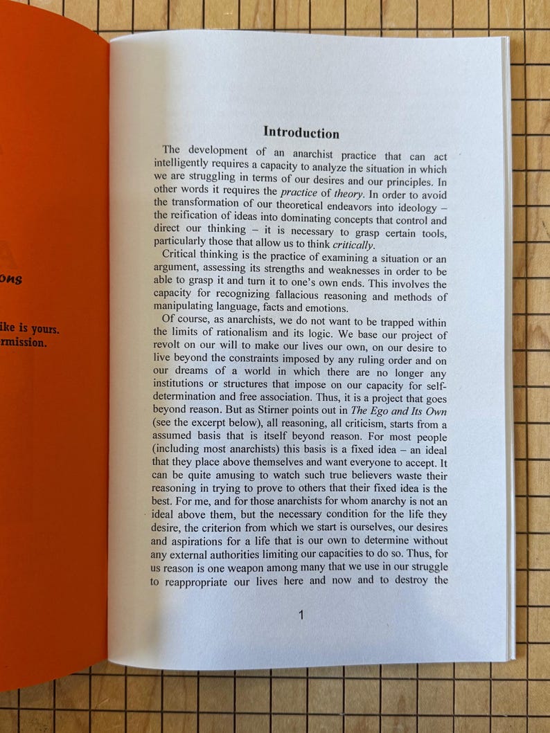 May include: An open book with a bright orange cover and white pages. The text on the page is about the development of anarchist practice and the importance of critical thinking.