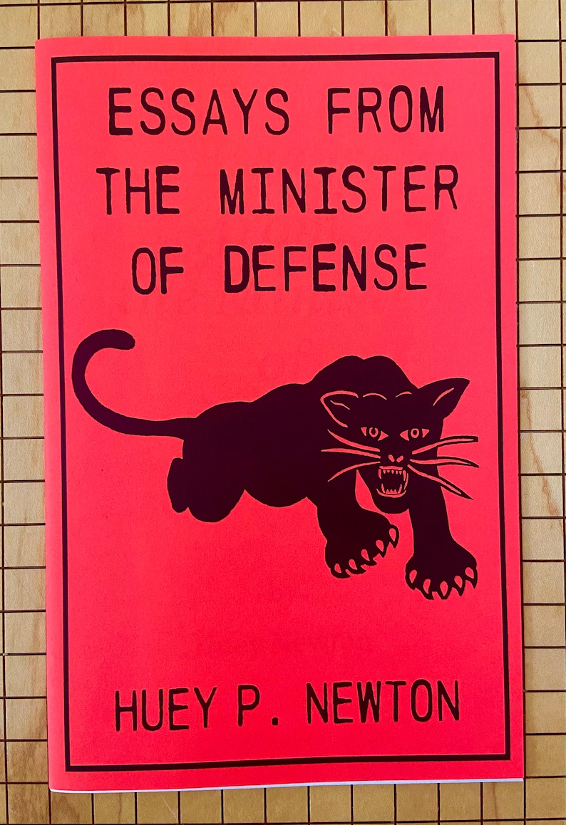 May include: A red book cover with black text that reads "Essays From The Minister Of Defense" and a black silhouette of a panther with a white face and white whiskers. The author's name, "Huey P. Newton", is printed in black at the bottom of the cover.