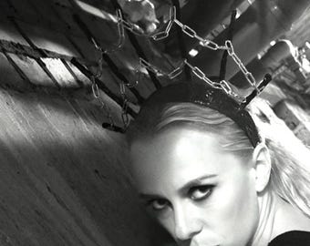 May include: A black headband featuring a halo-style crown constructed from silver-toned metal chains. The accessory is designed with multiple vertical spikes, each topped with a segment of chain, creating a structured, radiating circular frame.