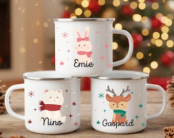 May include: Three white enamel mugs with silver rims, each featuring a different Christmas-themed design. One mug has a bunny, another a polar bear, and the third a reindeer. Each mug has a name printed on it: Emie, Nino, and Gaspard.