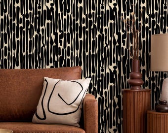 Puede incluir: Una escena de salón con un sofá de cuero marrón, un cojín blanco con un diseño abstracto negro y un papel pintado con estampado negro y beige. Una lámpara con pantalla beige y base de cerámica blanca se encuentra sobre una mesa auxiliar de madera.