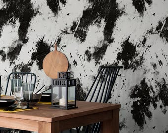Puede incluir: Un comedor con una mesa de madera puesta para una comida. Linternas y cubiertos negros contrastan con la madera clara. El fondo es una pared blanca con grandes salpicaduras de pintura negra y una alfombra estampada en blanco y negro.