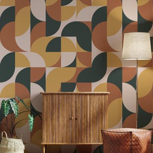 May include: A room with a mid-century modern design featuring a geometric wallpaper in shades of green, yellow, brown, and white. A wooden cabinet with vertical slats, a woven leather ottoman, a floor lamp, and a potted plant complete the scene.