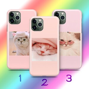 May include: Three light pink smartphone cases, each featuring a distinct cat photograph. Case 1 shows a cat in a pink hood, case 2 displays a sleeping cat under a pink blanket, and case 3 depicts a fluffy white cat wearing pink heart-shaped glasses.