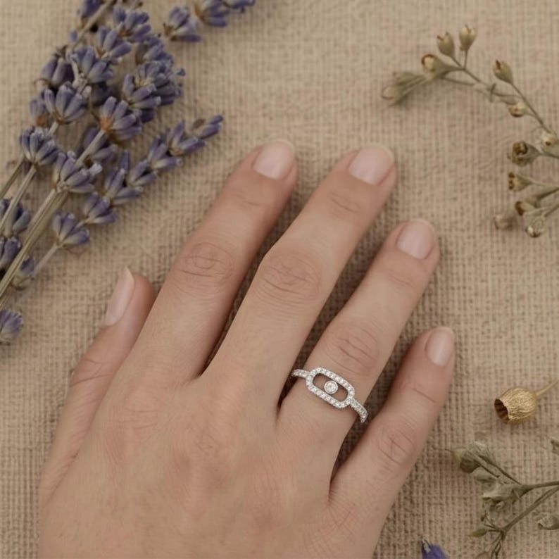 May include: A silver ring with a rectangular center design, encrusted with small, clear stones. A single, larger clear stone is set in the center of the rectangle. The ring is on a person's finger, with lavender and dried flowers in the background.