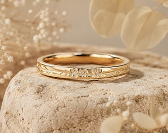Può includere: Un anello in metallo color oro caratterizzato da un delicato motivo floreale inciso che avvolge l'intera fascia. Il design è composto da piccoli fiori dettagliati e sottili foglie rampicanti incise sulla superficie del metallo lucido.