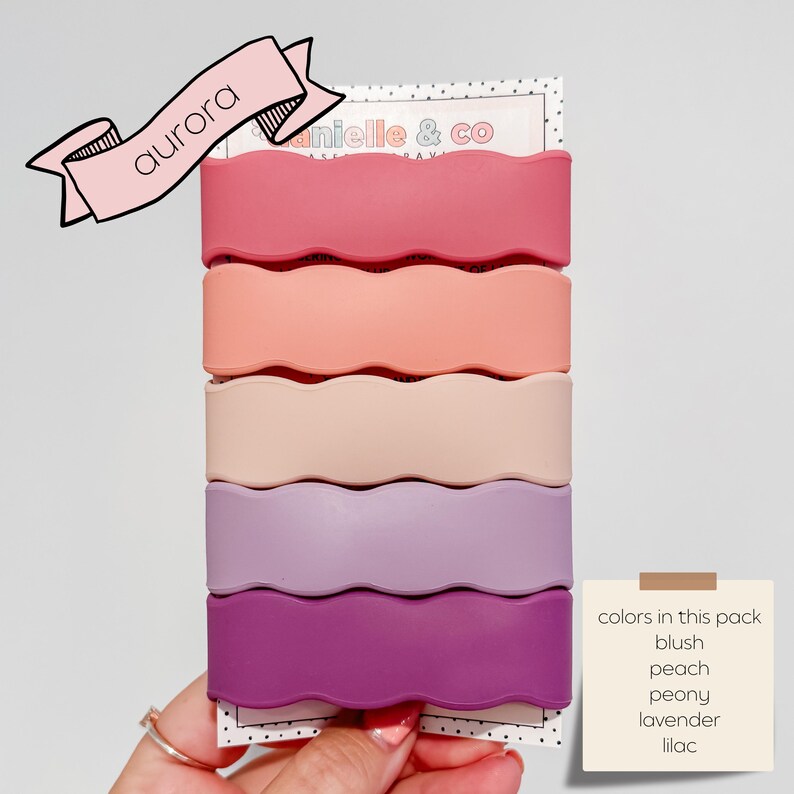 A hand holding a pack of five wavy hair clips in various pastel colors, including pink, peach, peony, lavender, and lilac.