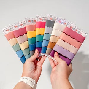 A person's hands holding a fan-like arrangement of colorful hair clips, each with a different color.