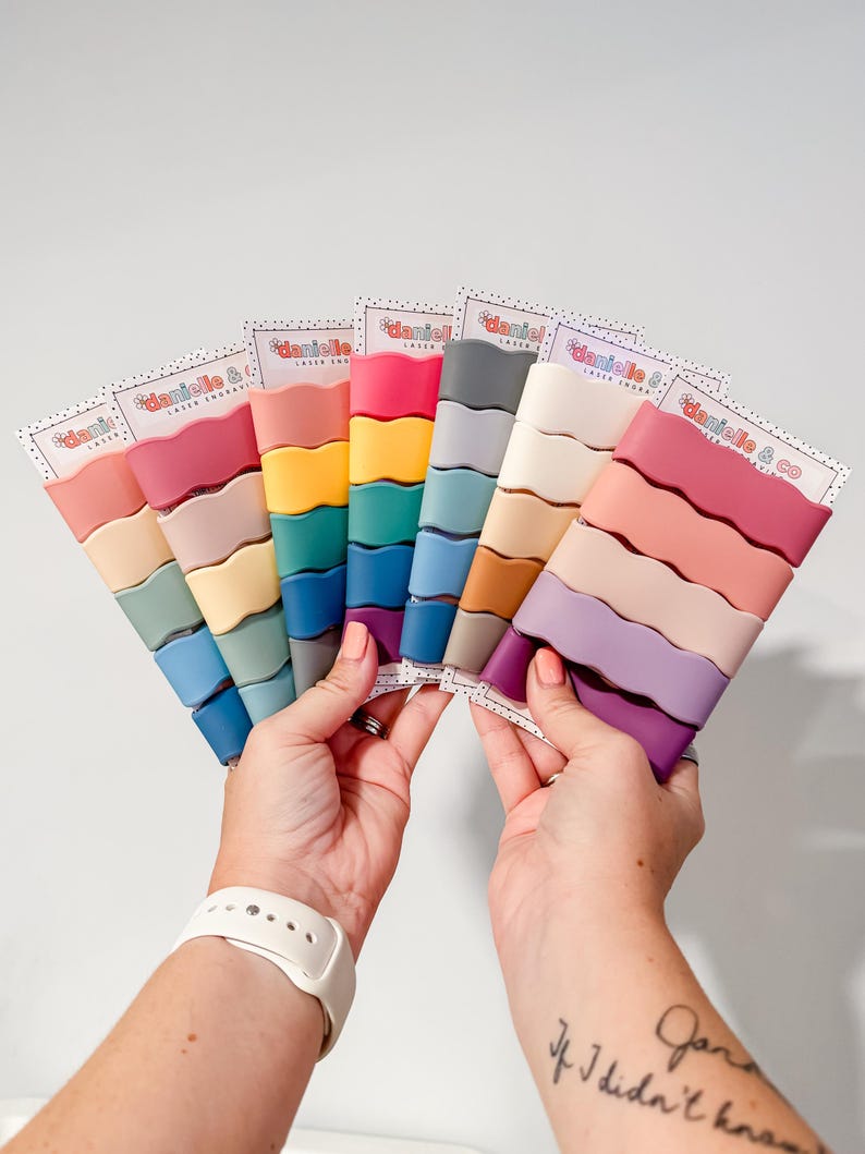 A person's hands holding a fan-like arrangement of colorful hair clips, each with a different color.