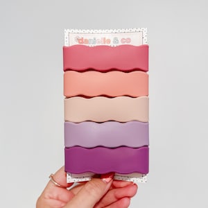 A hand holding a set of colorful hair clips in a row.