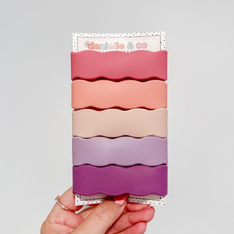 A hand holding a set of colorful hair clips in a row.