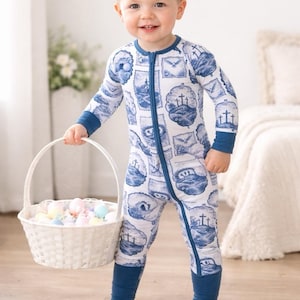 K&ouml;nnte beinhalten: Ein Kleinkind in einem wei&szlig;-blau gemusterten Strampler mit Rei&szlig;verschluss h&auml;lt einen wei&szlig;en Weidenkorb mit pastellfarbenen Ostereiern. Der Strampler hat einen blauen Aufdruck mit Kreuzen und anderen Designs.