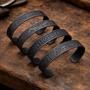 May include: Four dark gray metal cuff bracelets with intricate engraved designs, including runes and Celtic knot patterns. The bracelets are arranged in a spiral on a wooden surface, showcasing their detailed craftsmanship and Viking theme.