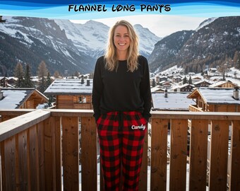 Könnte beinhalten: Eine Person trägt ein schwarzes Langarmshirt und eine rot-schwarz karierte Flanellhose. Auf der Hose steht der Name "Candy". Im Hintergrund sind schneebedeckte Berge und ein Dorf zu sehen.