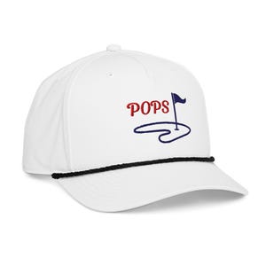 May include: A white baseball cap featuring an embroidered design with the red text POPS next to a dark blue golf flag and hole graphic. The cap includes a black braided cord trim across the base of the crown, just above the curved visor.