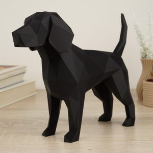 Op de afbeelding: Een zwarte geometrische hondensculptuur met een polygonale vormgeving. De hond staat op vier poten met zijn staart omhoog. De sculptuur is gemaakt van een matzwart materiaal en staat op een lichtgekleurd houten oppervlak.