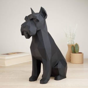 Peut inclure: Une figurine de chien noir mat au design géométrique et low-poly. La sculpture représente un canidé assis avec des oreilles pointues et un museau distinct, construit à partir de multiples plans angulaires plats créant un aspect facetté.