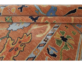 May include: Close-up of a rolled-up rug with an intricate pattern. The rug has a warm orange-red base with floral and geometric designs in blue, green, yellow, and black. The texture of the woven rug is clearly visible.