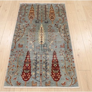 May include: A rectangular, hand-knotted rug with a light blue background and a detailed tree and animal design. The rug features trees with brown and red leaves, and small animal figures. The rug is placed on a light wood floor.