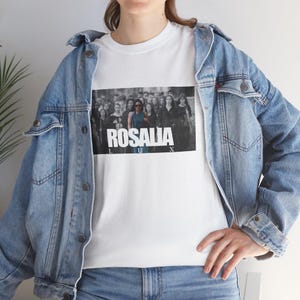 May include: White t-shirt featuring a black and white image of a crowd with the word "ROSALIA" in bold white letters. The shirt is worn with a light blue denim jacket.