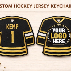 May include: Custom hockey jersey keychains in black and gold. One keychain has the name "KEMP" and the number "1". The other has space for a logo. Both have white stripes.