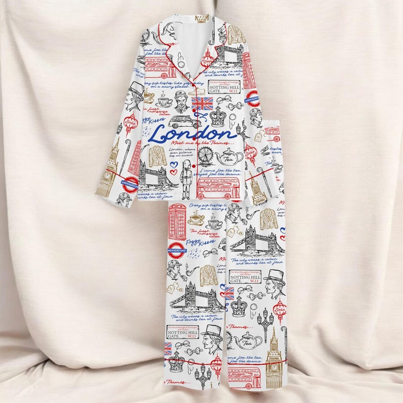 May include: White London-themed pajama set featuring a button-down top and trousers. The print includes iconic landmarks, the word "London", and red trim. The set is designed for comfort and style.